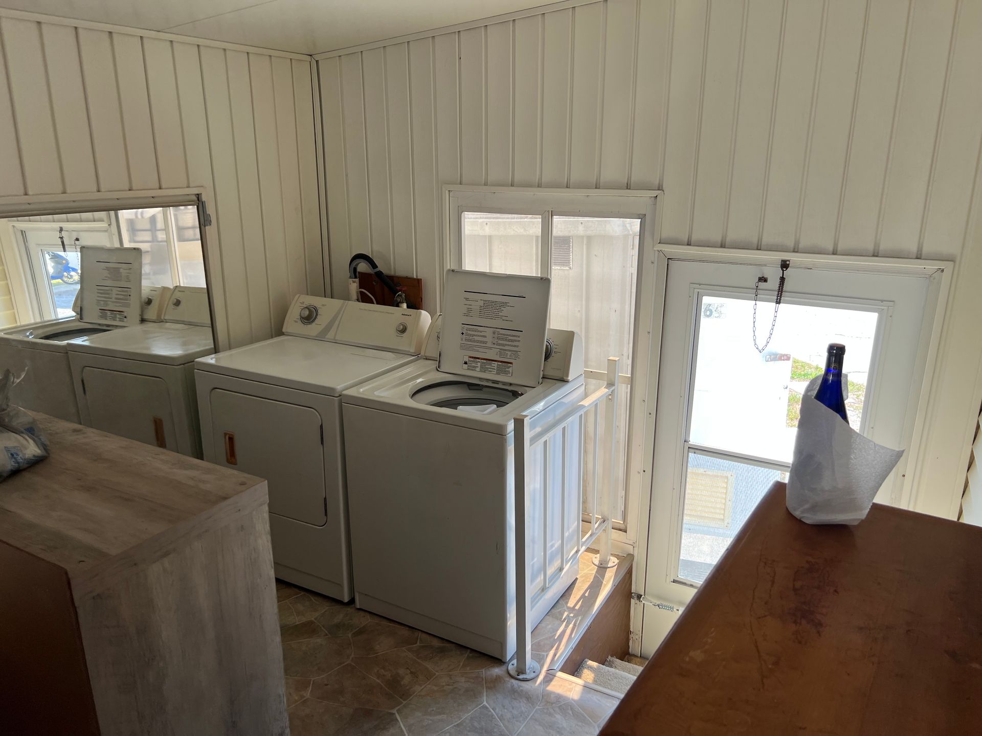 White laundry room with a washer and dryer, a wooden counter, and a glass door leading outside.
