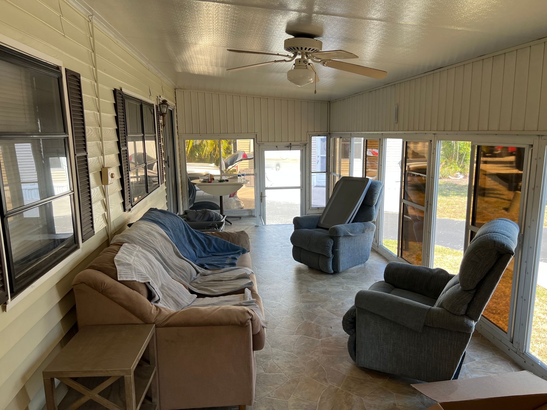 A sunroom featuring light yellow walls, a tan couch, two blue reclining chairs, and a ceiling fan.
