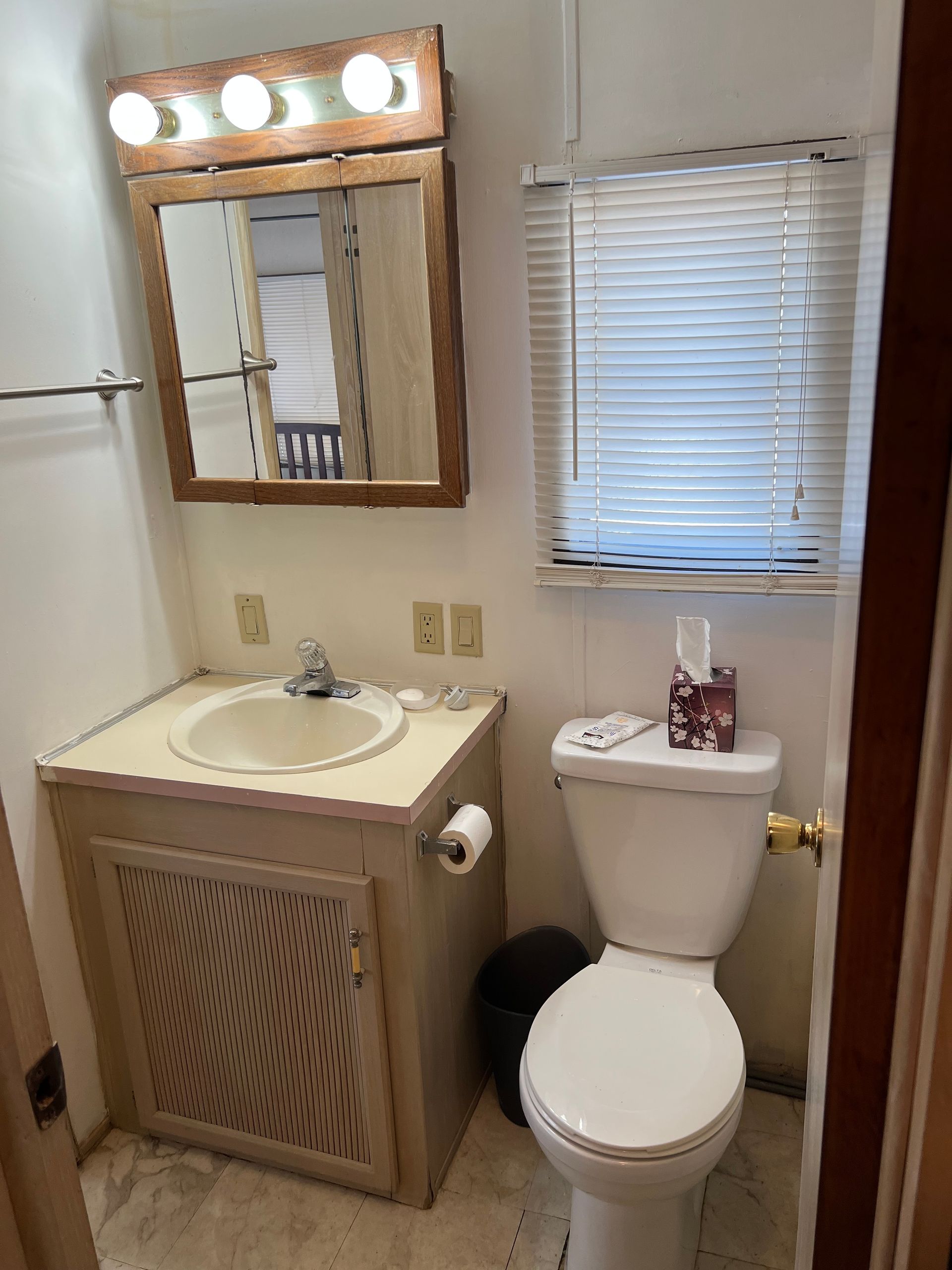 A small, functional bathroom with a light-colored sink vanity, a wooden medicine cabinet mirror, and a white toilet.