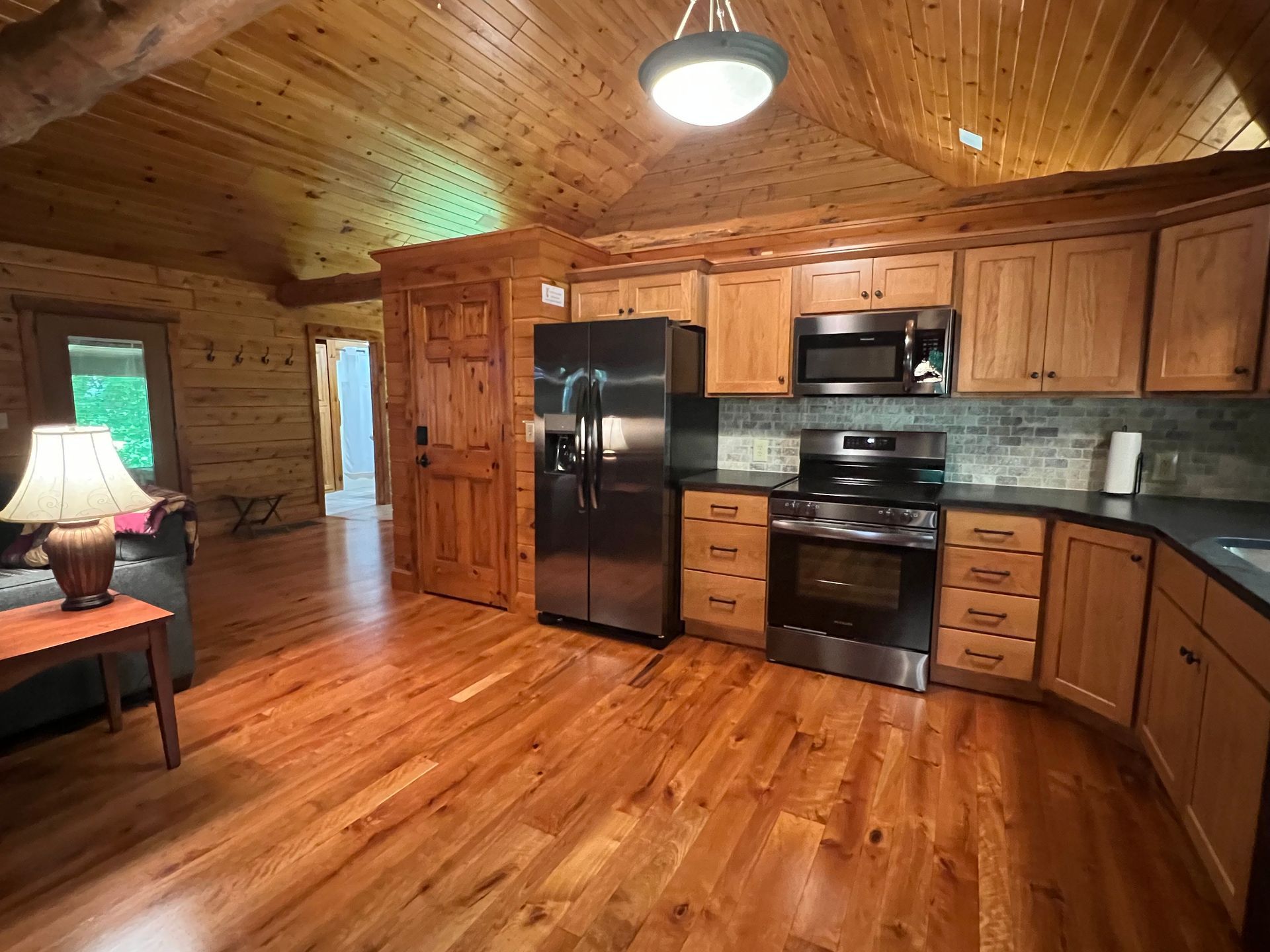 A rustic cabin interior featuring a wooden kitchen with stainless steel appliances, open-concept living, and warm lighting.