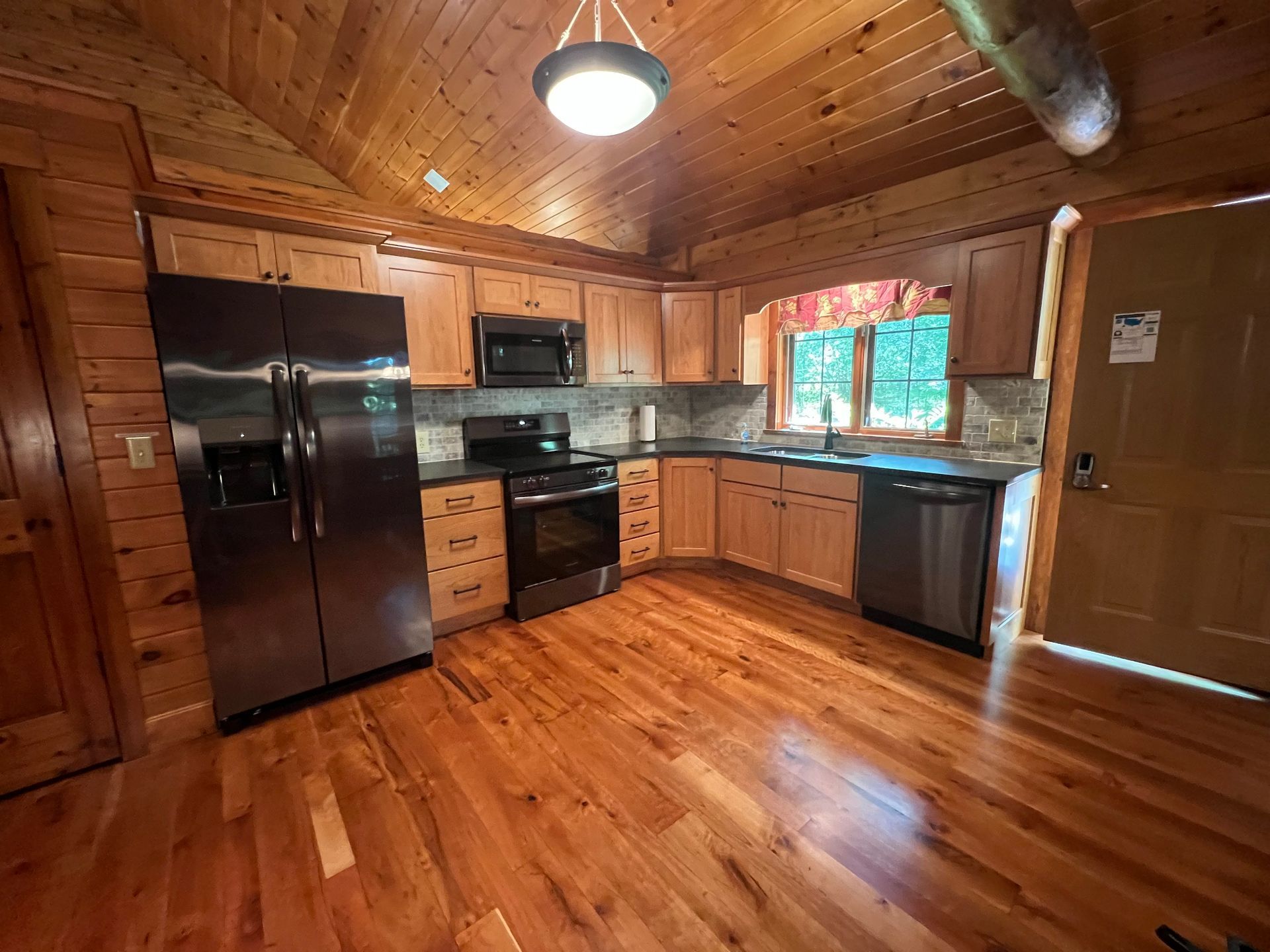 A rustic log cabin kitchen with light wooden cabinets, stainless steel appliances, and dark countertops.