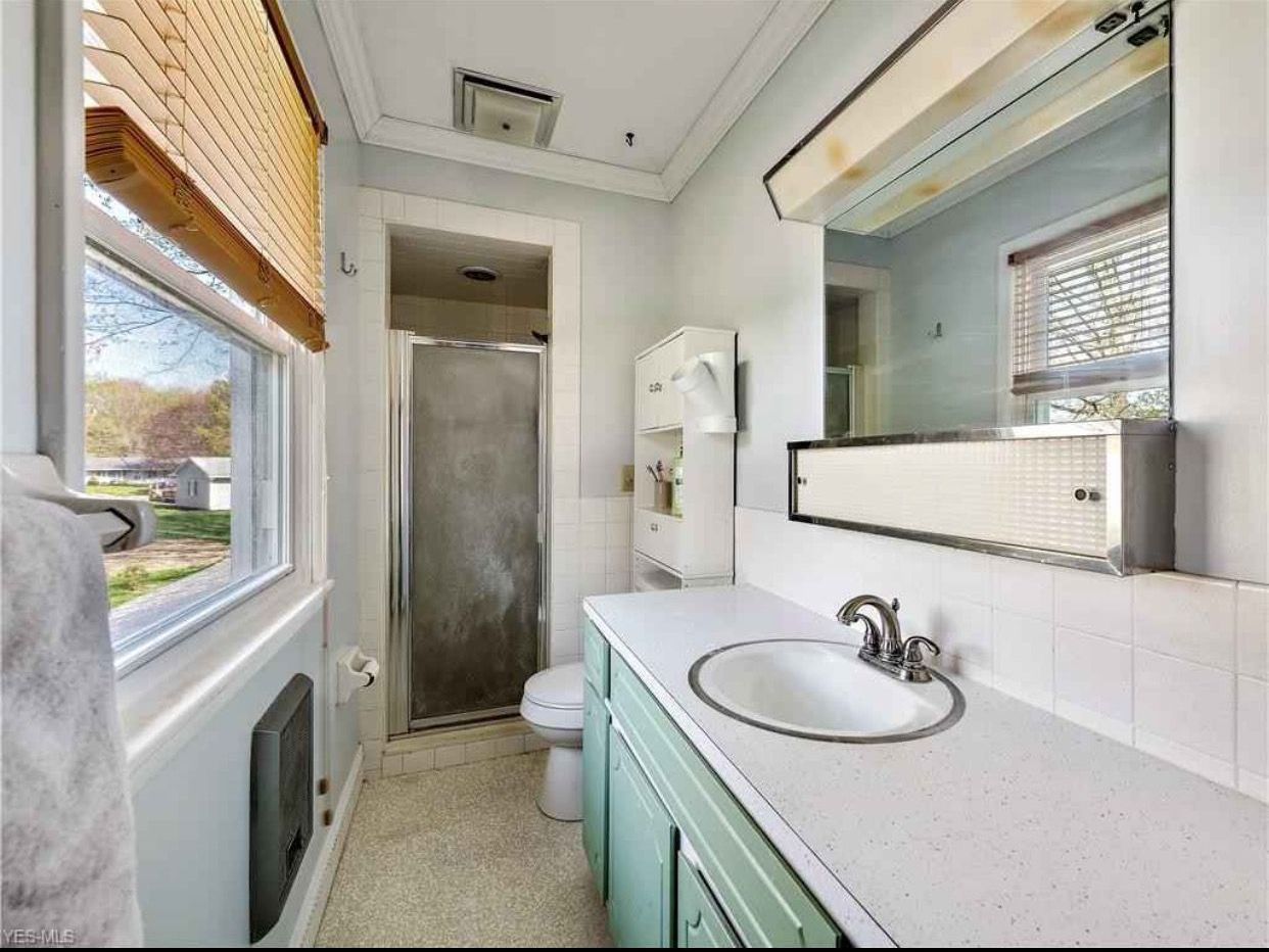 A bathroom with a white vanity, a round sink, a mirror with cabinet storage, a toilet, and a glass-enclosed shower.