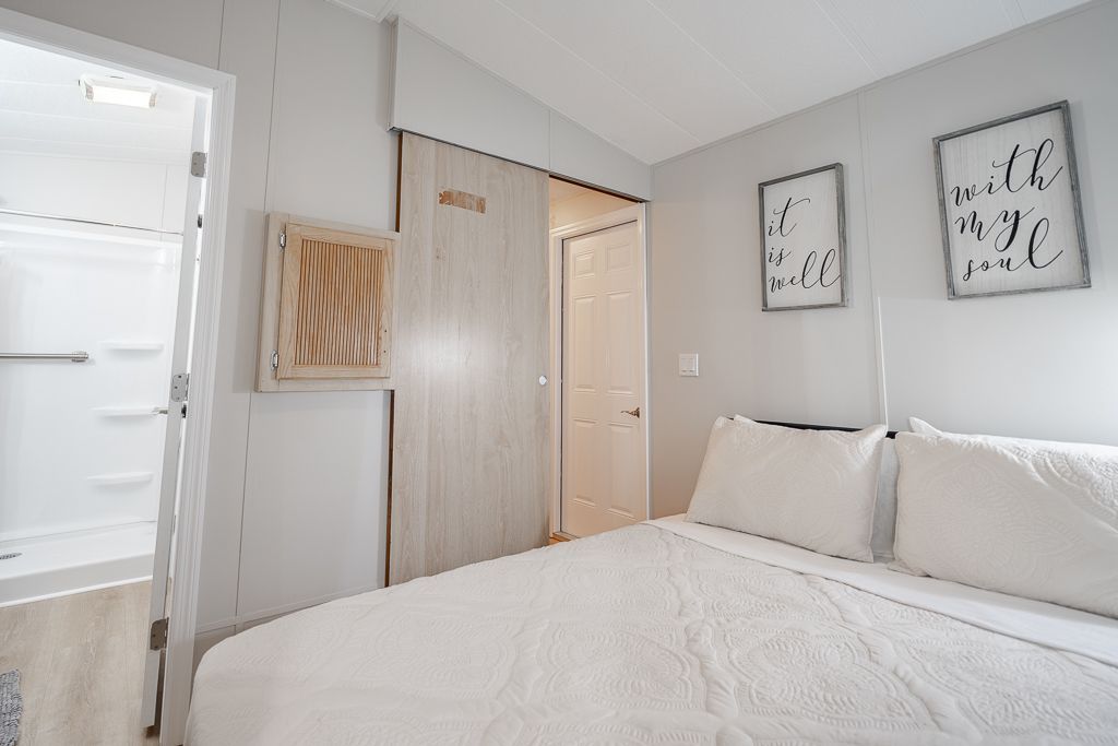 A bedroom with a bed featuring white bedding, a sliding light wood door, a bathroom door, and two framed wall signs.