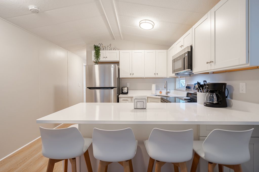 A modern kitchen with white cabinets, stainless steel appliances, a white quartz island, and four stools.