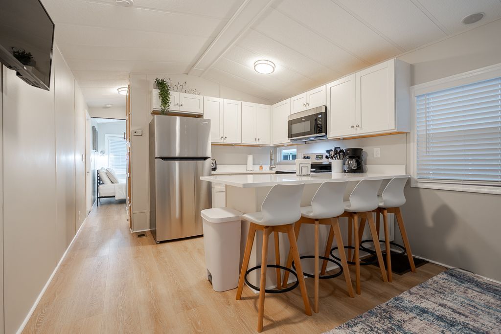 Modern kitchen featuring white cabinets, stainless steel appliances, and a breakfast bar with four stools.