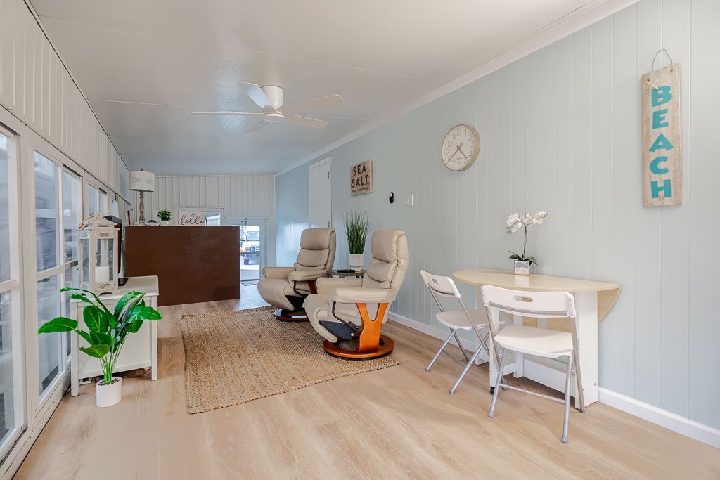 A light-colored sunroom with two recliners, a small dining table with two white chairs, and a 