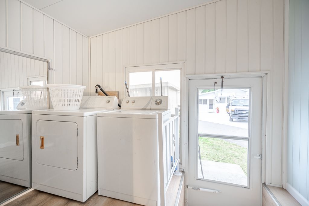 A laundry room featuring two white washing machines, a white laundry basket on top, and a white door leading outdoors.