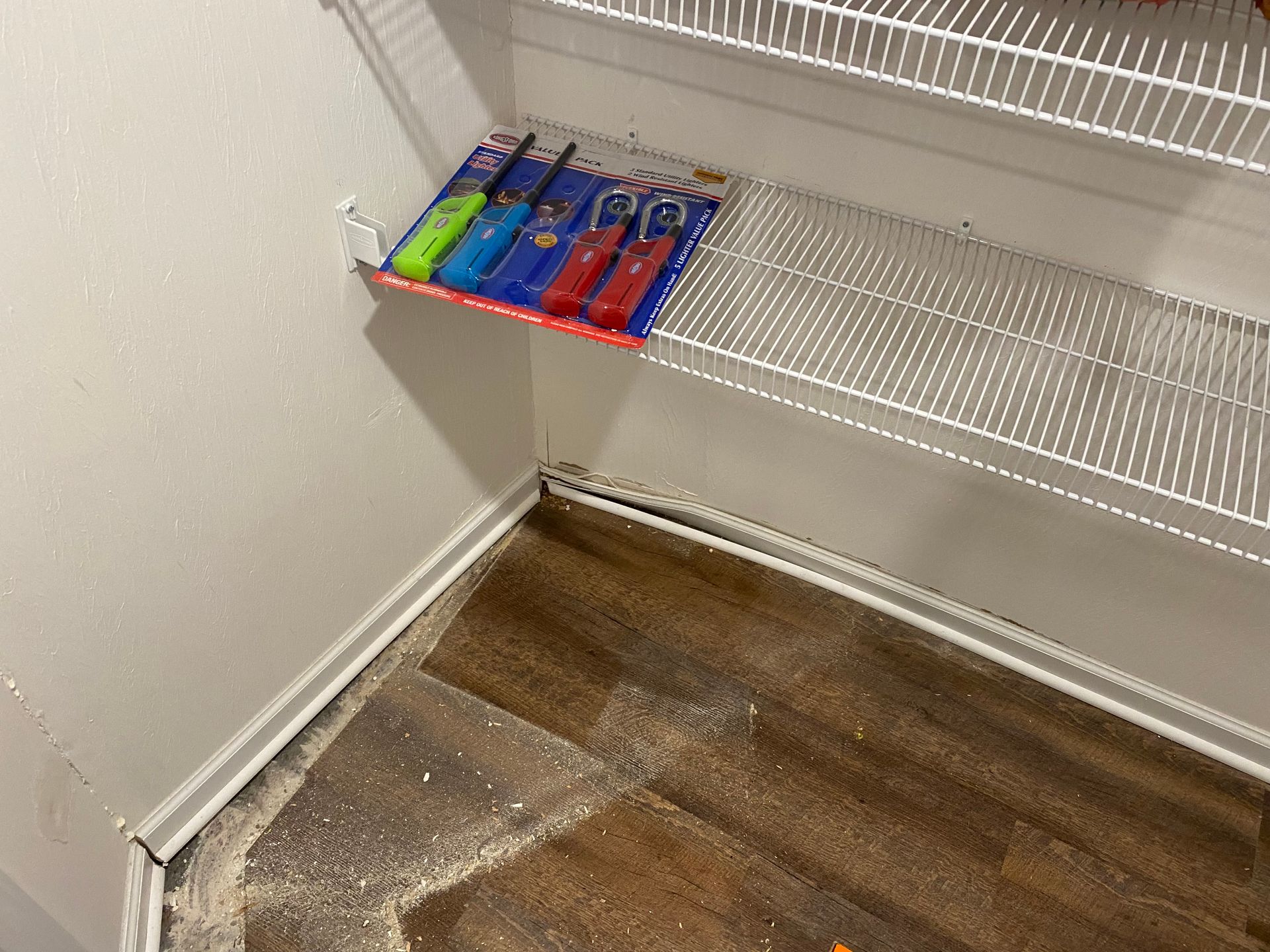 A pack of colorful utility lighters resting on a white wire shelf in a pantry with wood-look flooring.