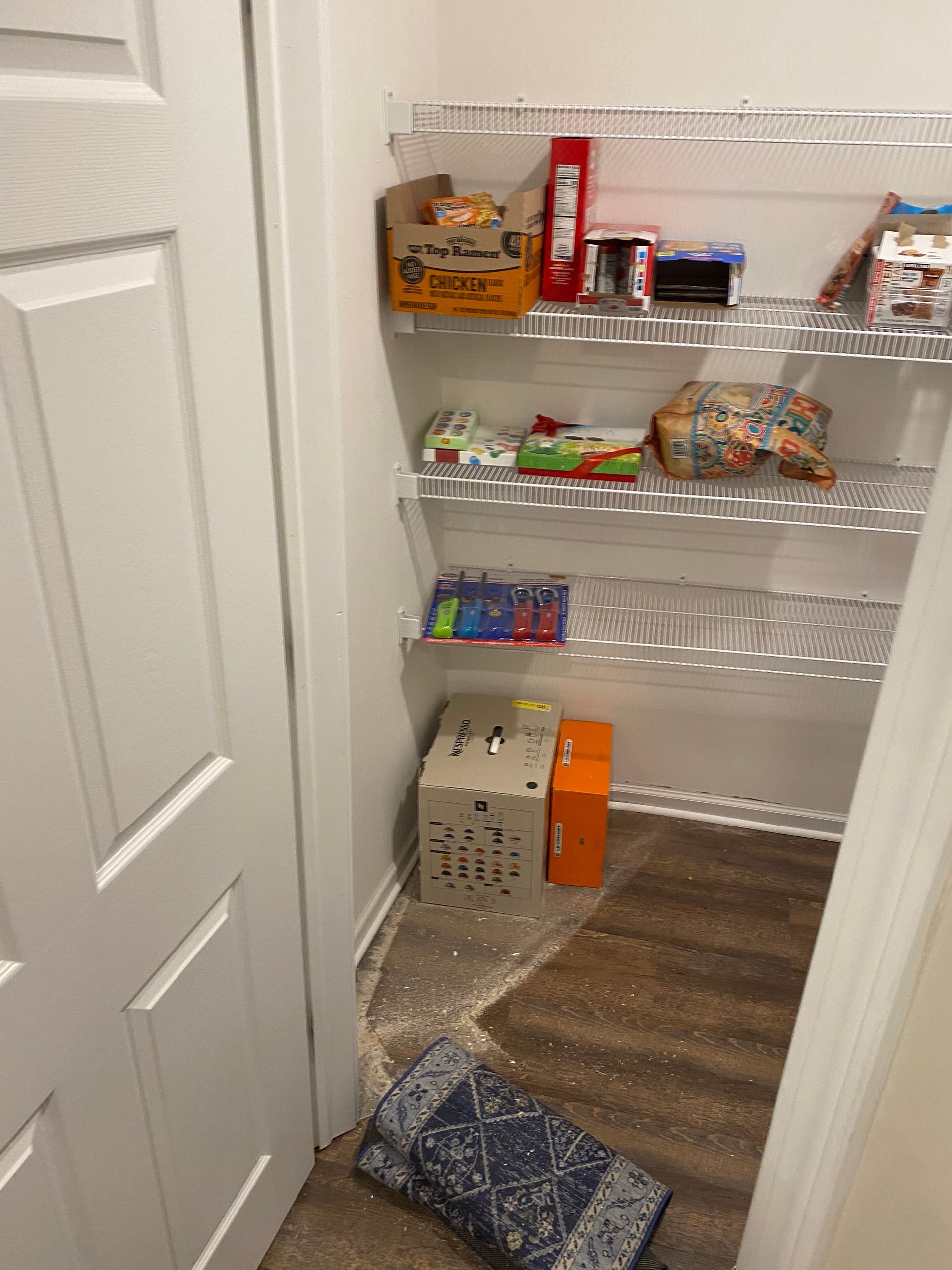 A pantry with wire shelving holding various food items, with spilled dry goods and a folded rug on the floor.