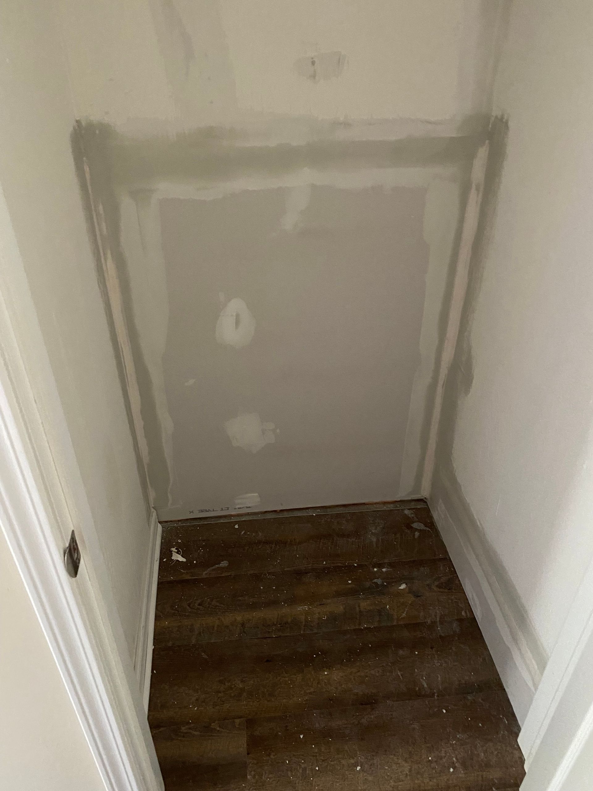 A small, unfinished closet interior with bare drywall, taped joints, and exposed wood flooring.