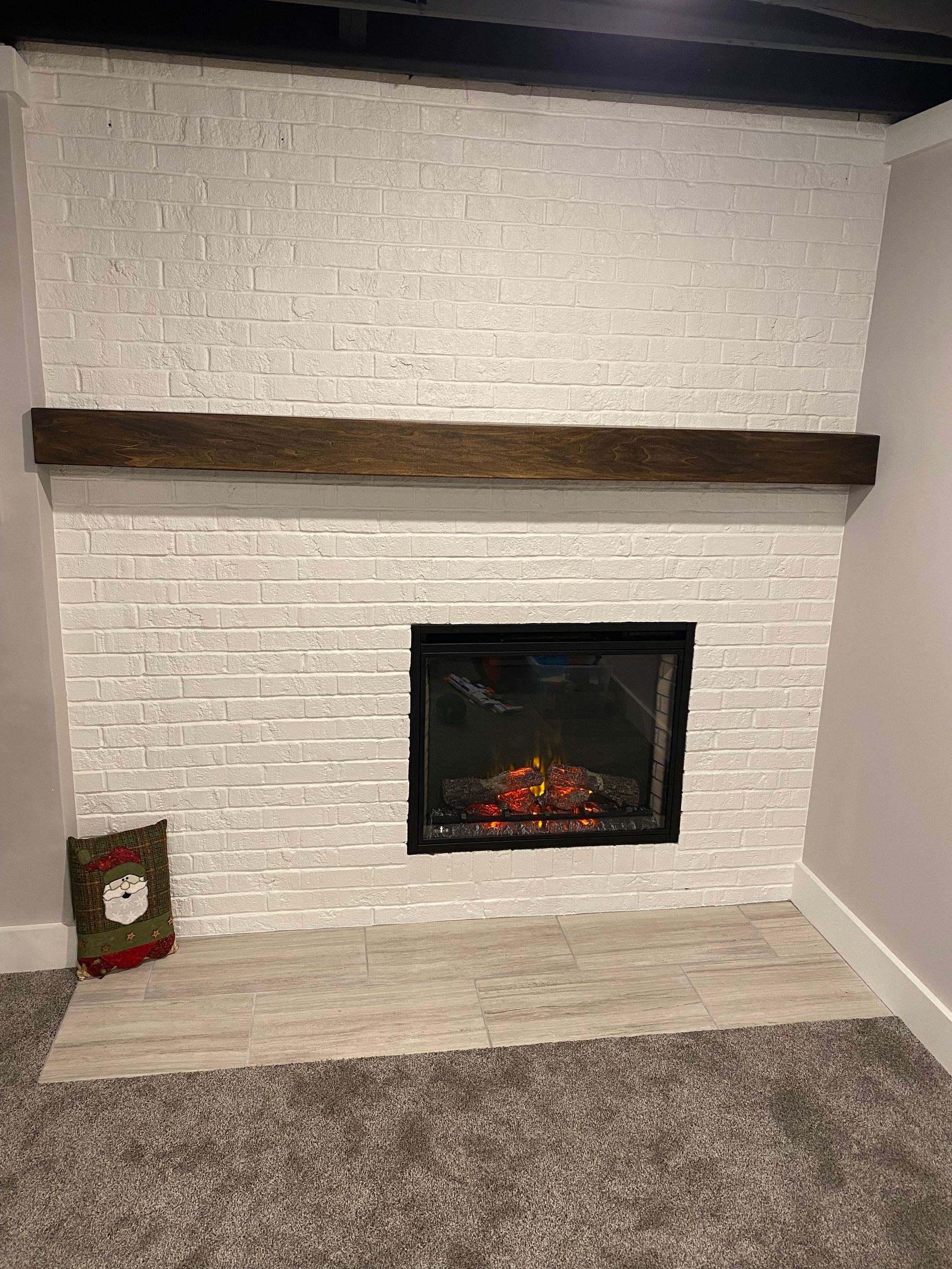 A white brick fireplace with a dark wood mantel and electric fire insert, featuring a small Christmas decor item.