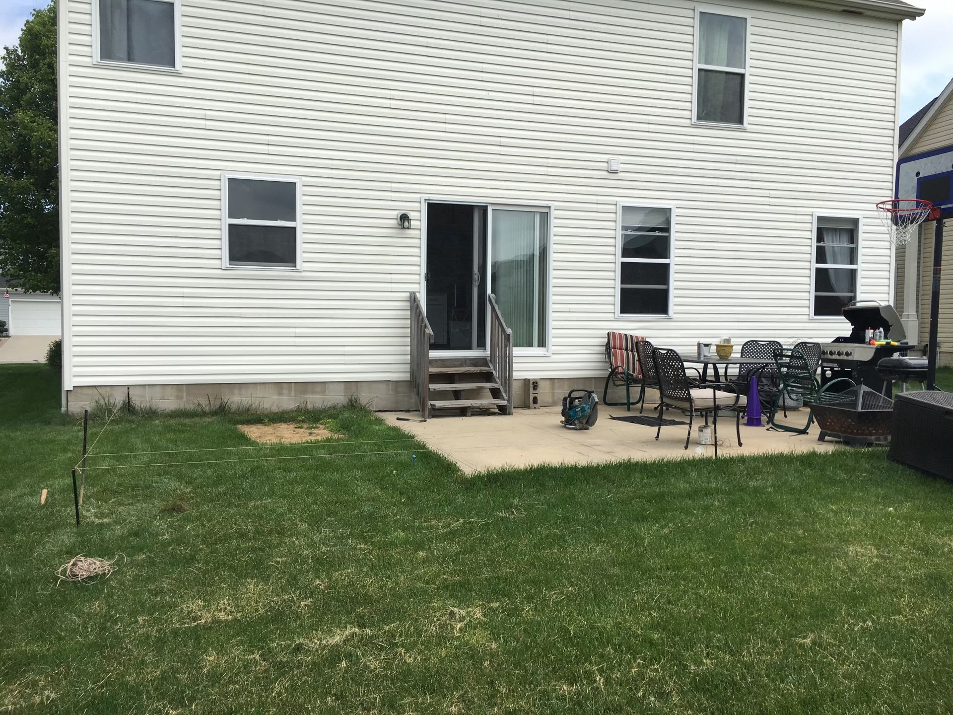 A white two-story house with a small concrete patio, sliding glass door, and a grill set up in the backyard.