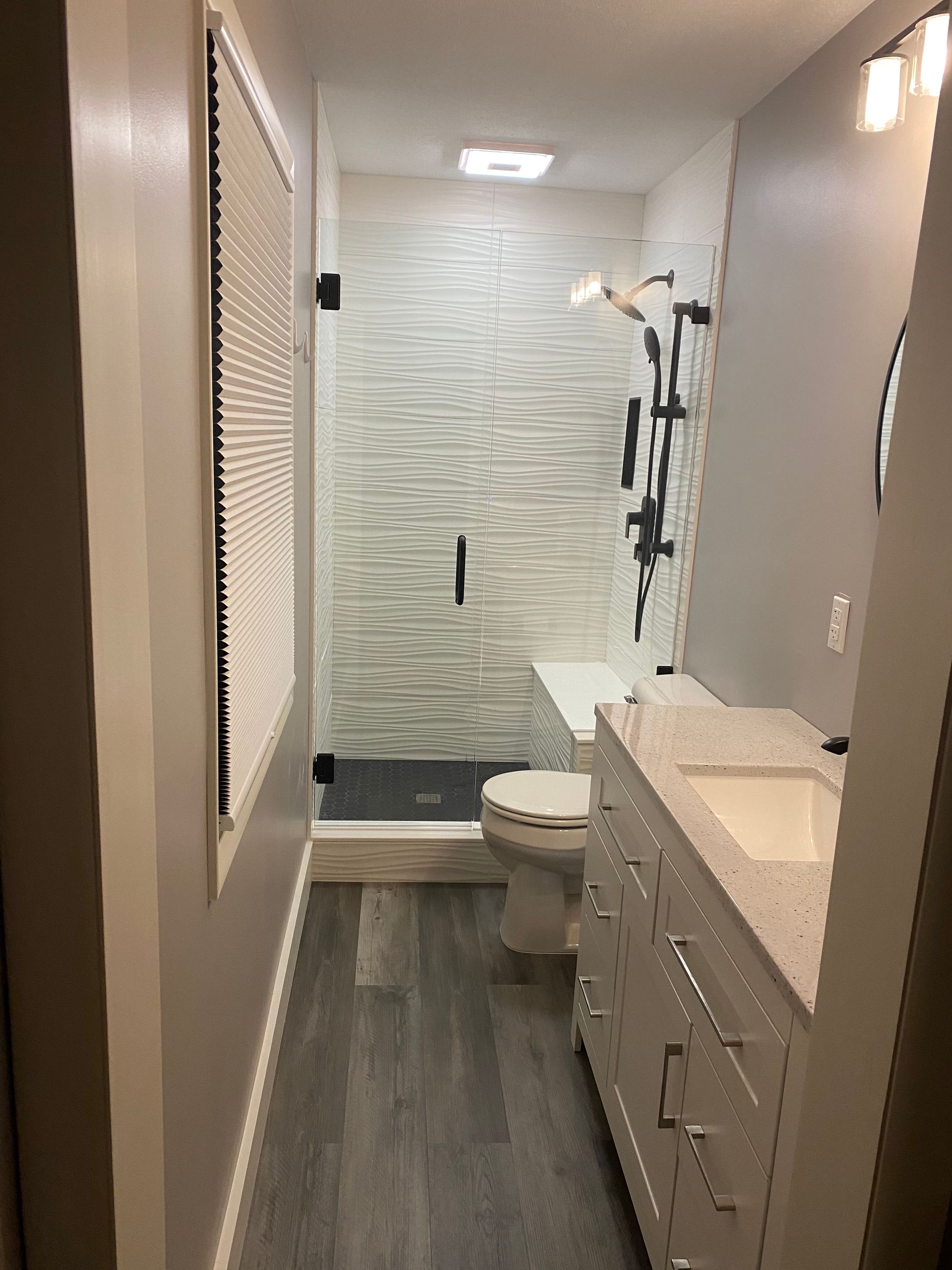 Modern bathroom with a white vanity, a grey toilet, and a glass-enclosed shower with textured white tile walls.