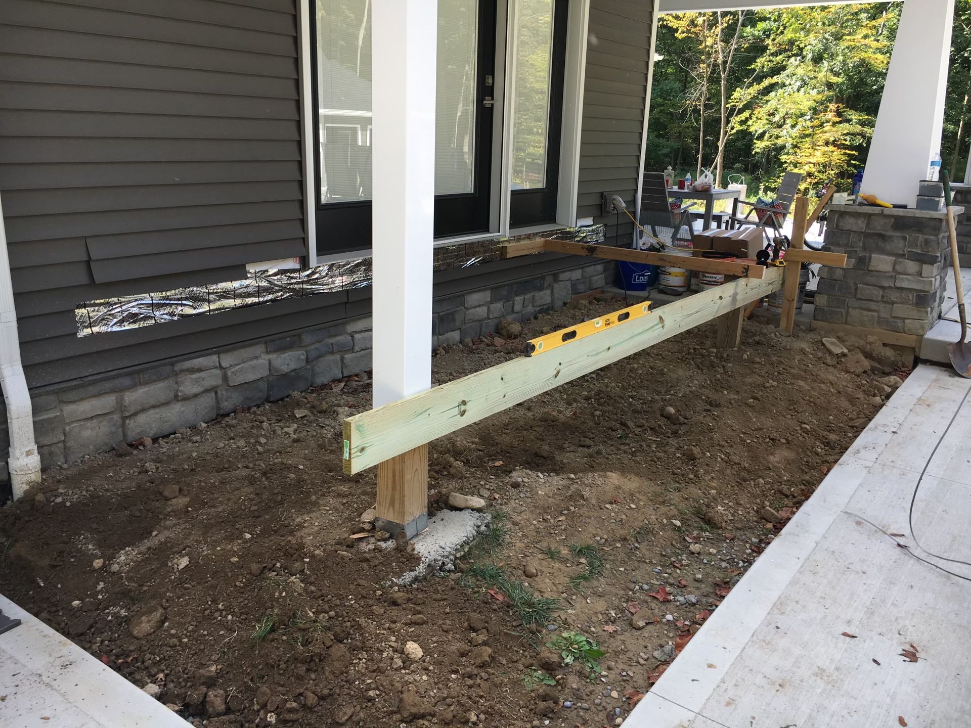 A level rests on a wooden beam supported by a post in front of a house under construction.