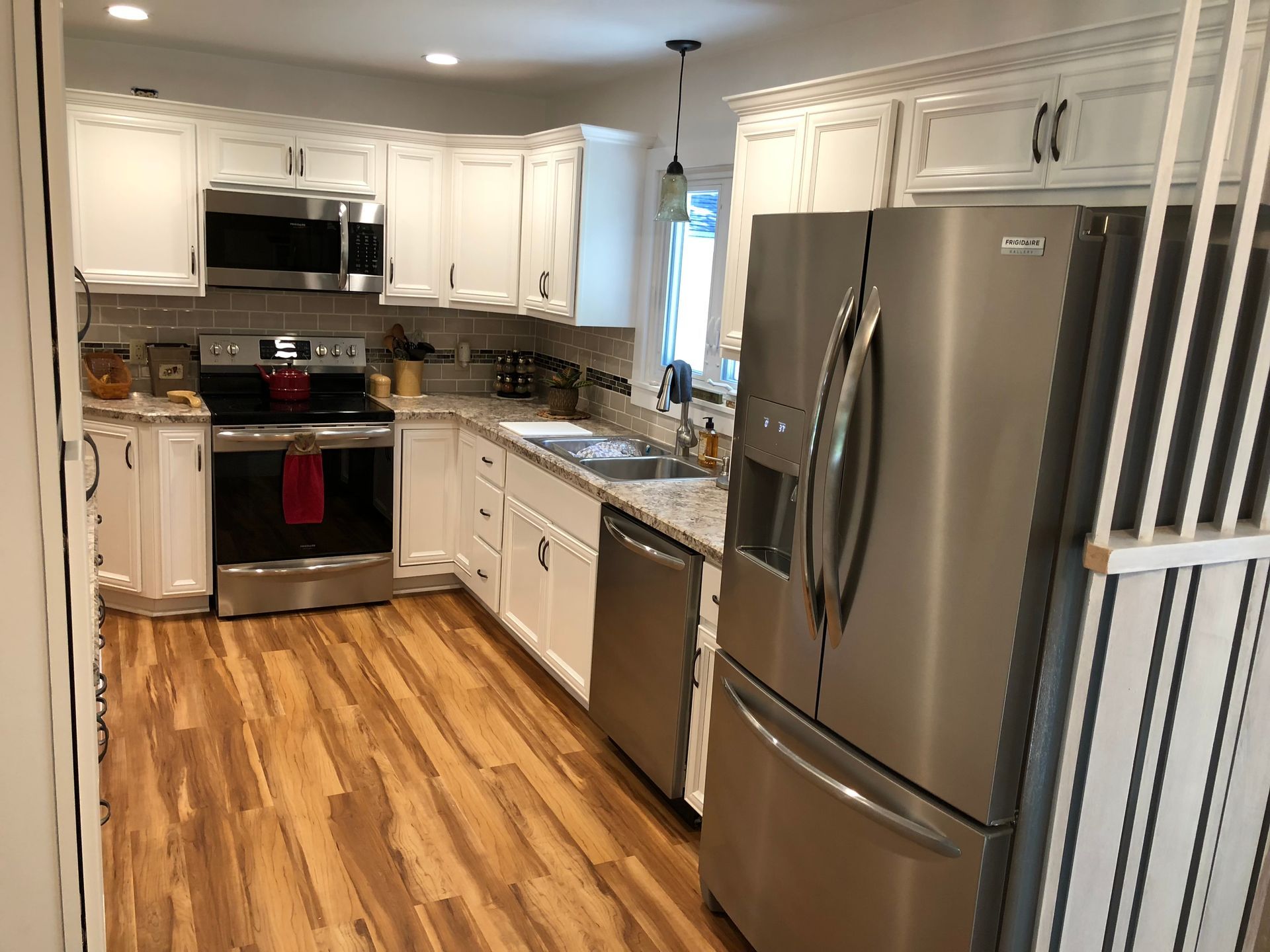 A modern kitchen with white cabinets, stainless steel appliances, speckled countertops, and wood-patterned flooring.
