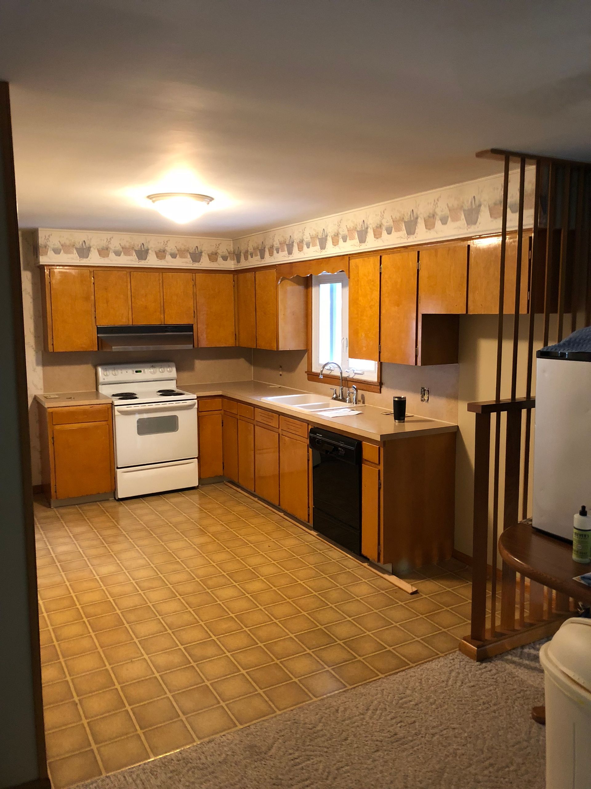 A kitchen with honey-oak cabinets, a white stove, black dishwasher, and patterned flooring under a decorative border.