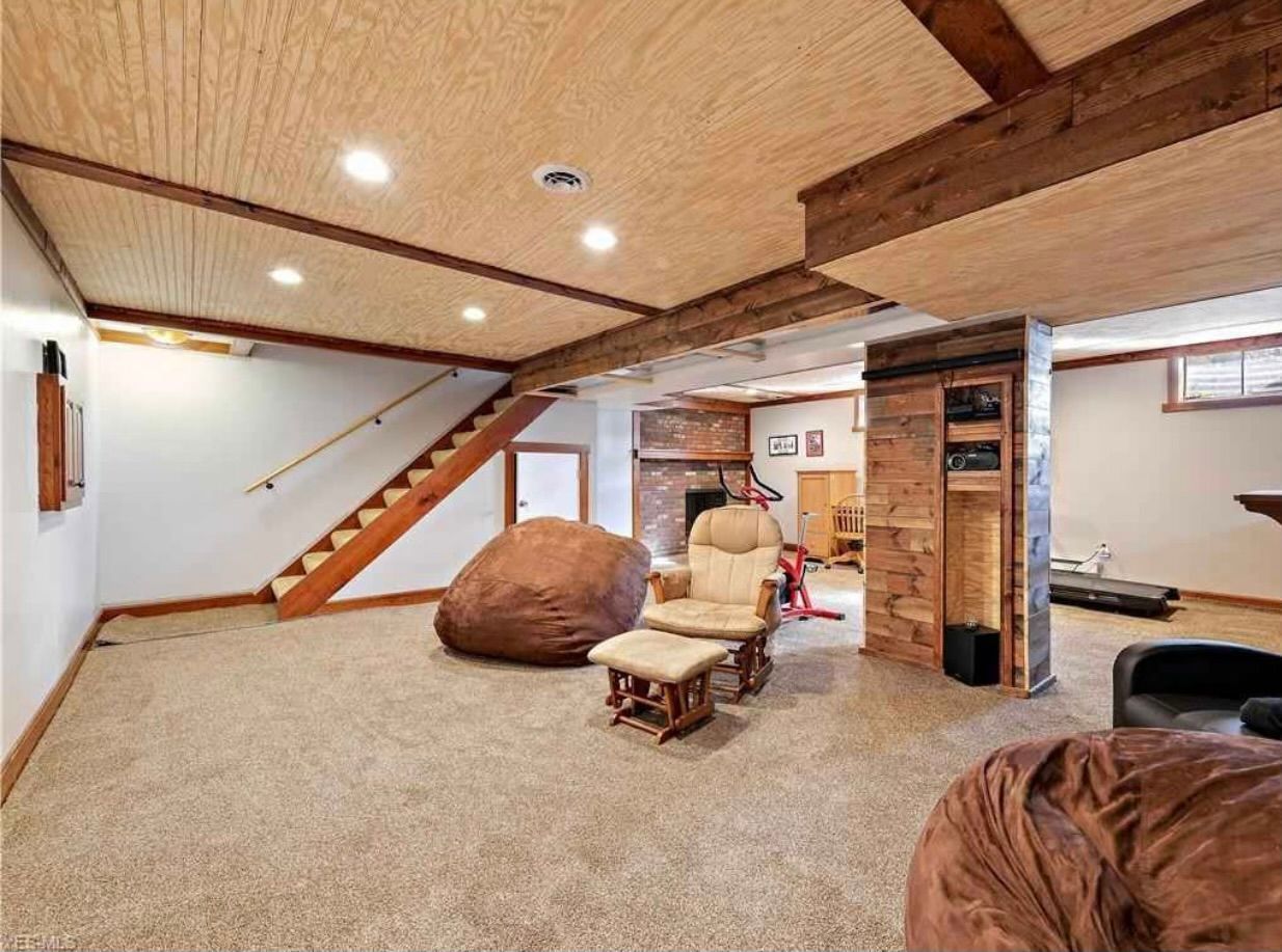 A finished basement with a wooden ceiling, carpeted floors, stairs, a fireplace, and casual seating like beanbags.