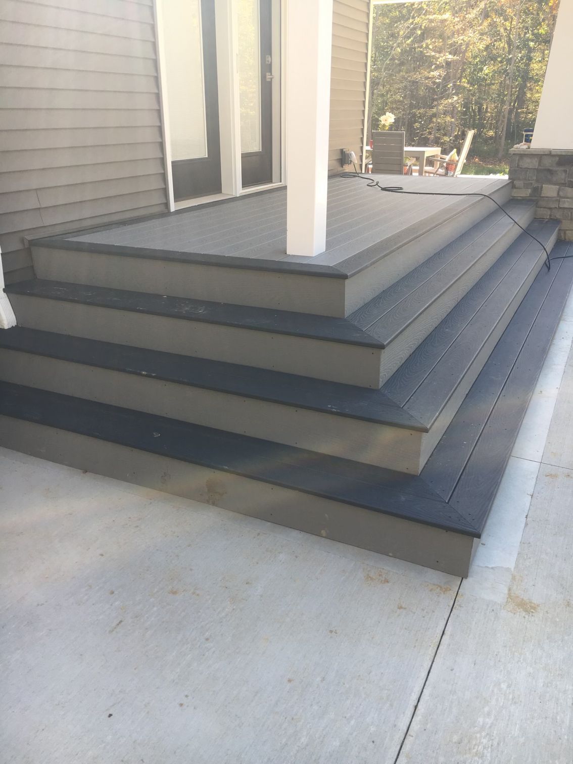 A set of three dark gray wooden steps leading up to an exterior doorway on a light-colored house.