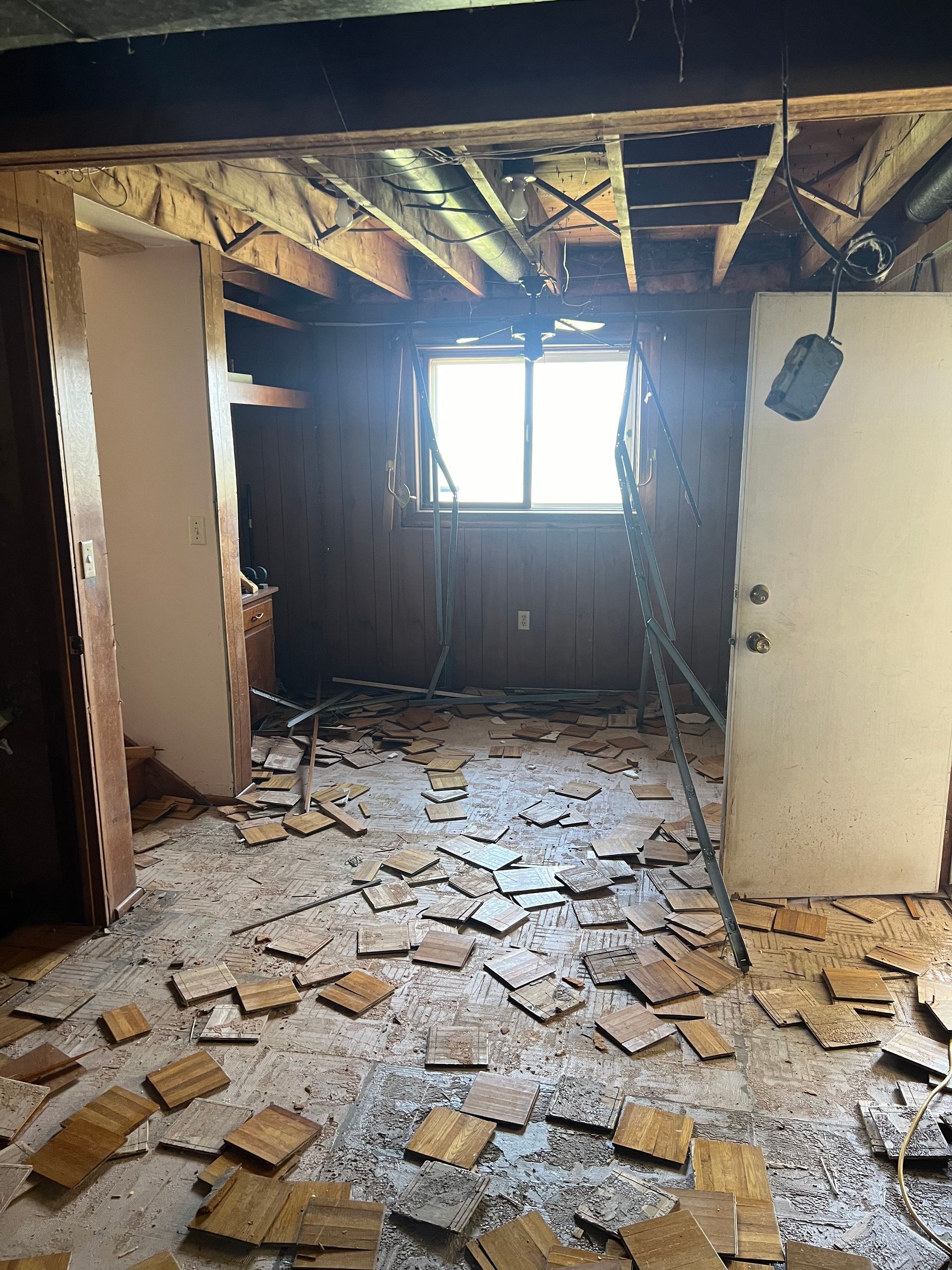 A room under renovation with a missing ceiling, exposed wooden beams, and debris scattered across the floor.