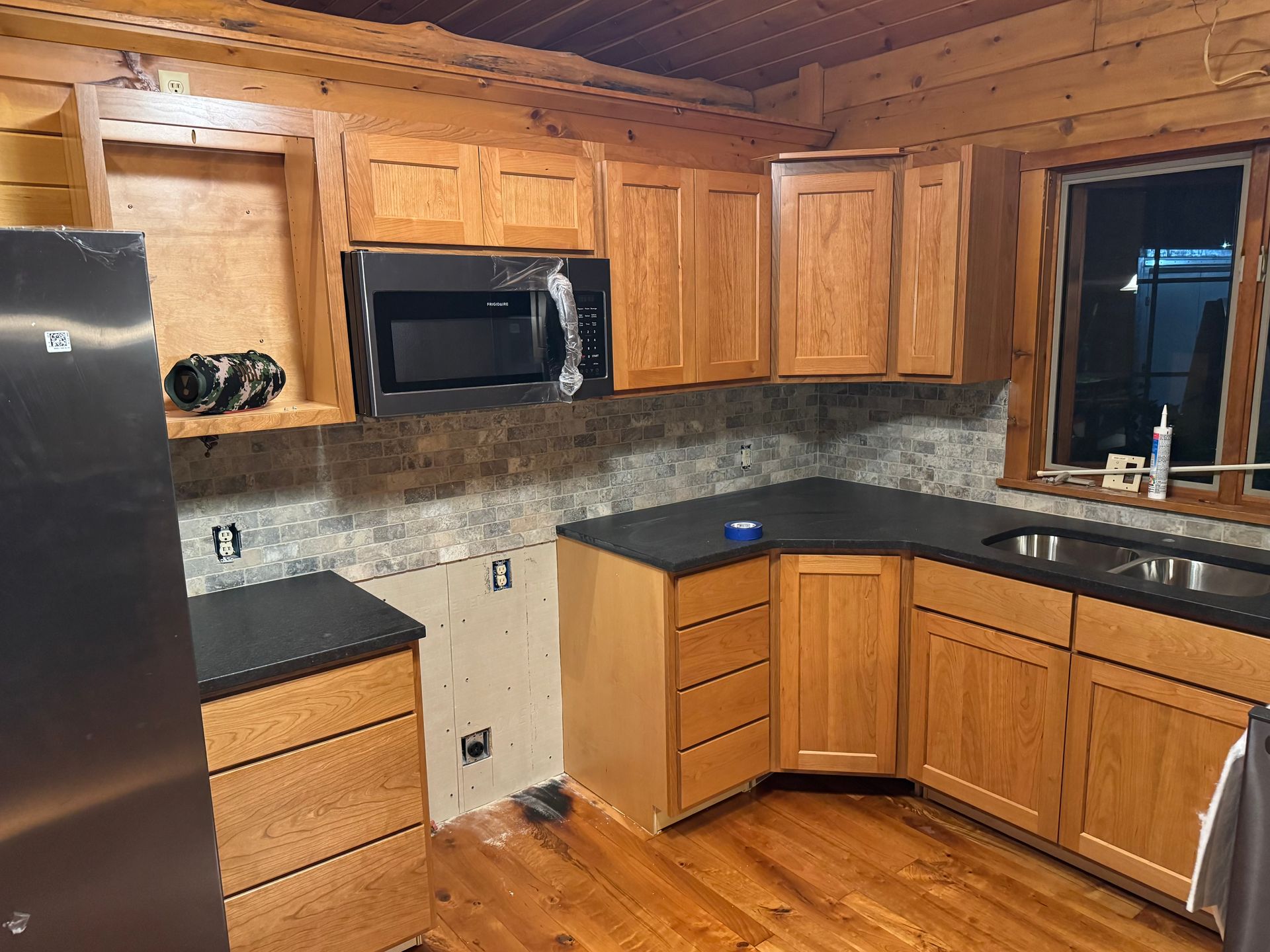 A kitchen under renovation with wooden cabinets, a dark countertop, stainless steel appliances, and unfinished backsplash.