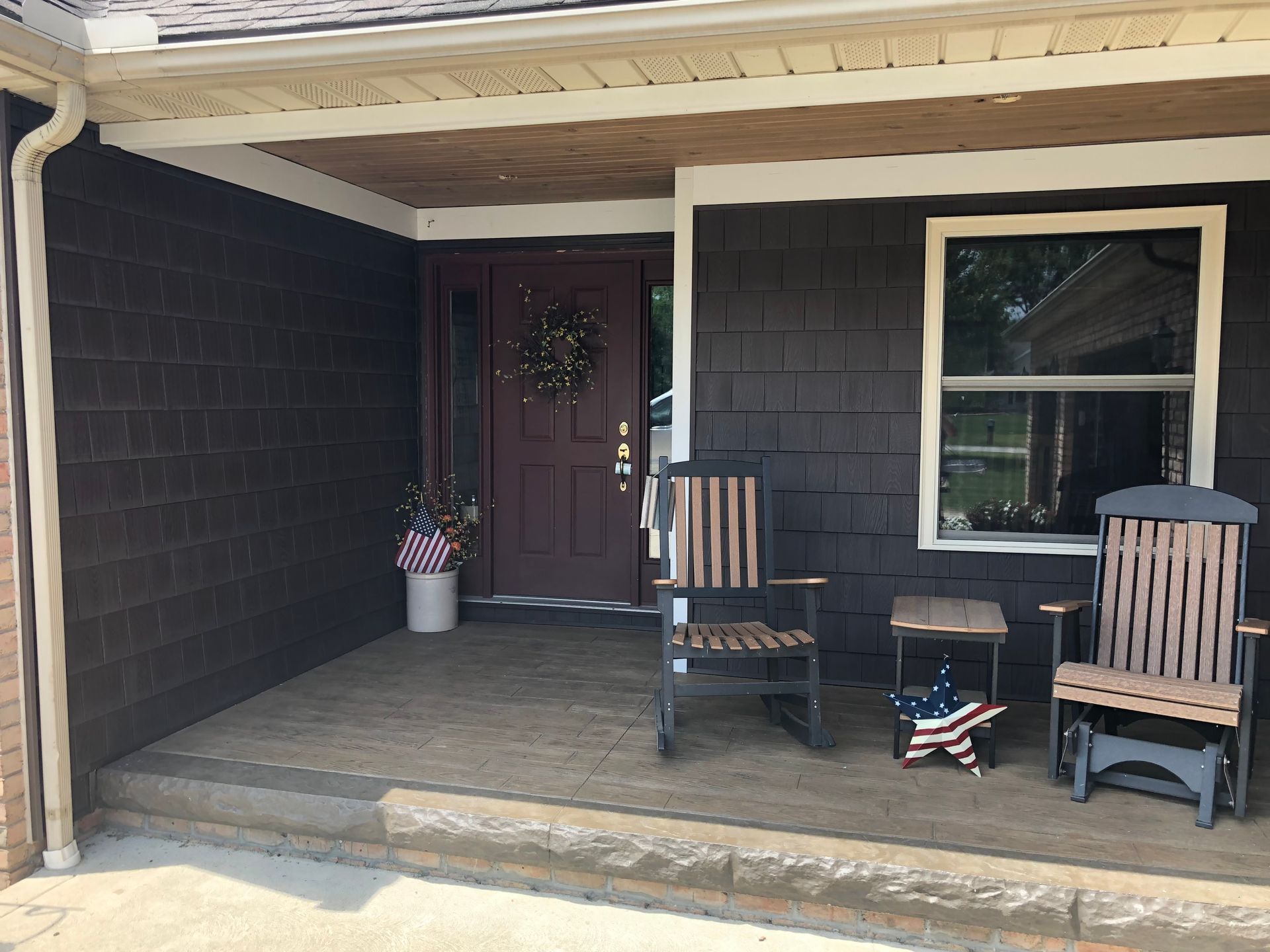 A dark-painted front porch with two wooden rocking chairs, a small table, and patriotic decor near the entry door.