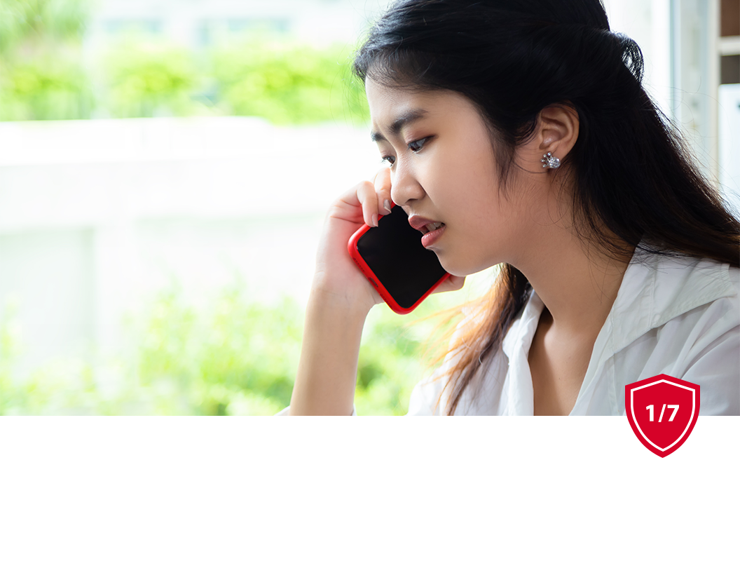 A person talking on a red smartphone near a window with a blurred green background.