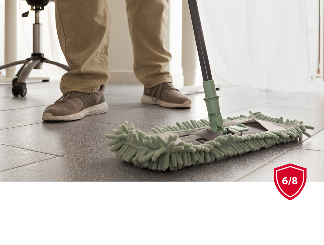 A person in beige pants and sneakers mops a gray tiled floor with a light green microfiber mop head.