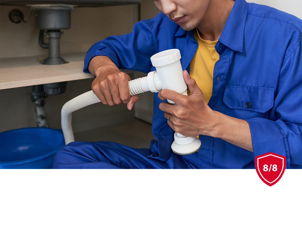 A plumber in a blue uniform assembling white plastic plumbing pipes under a sink.