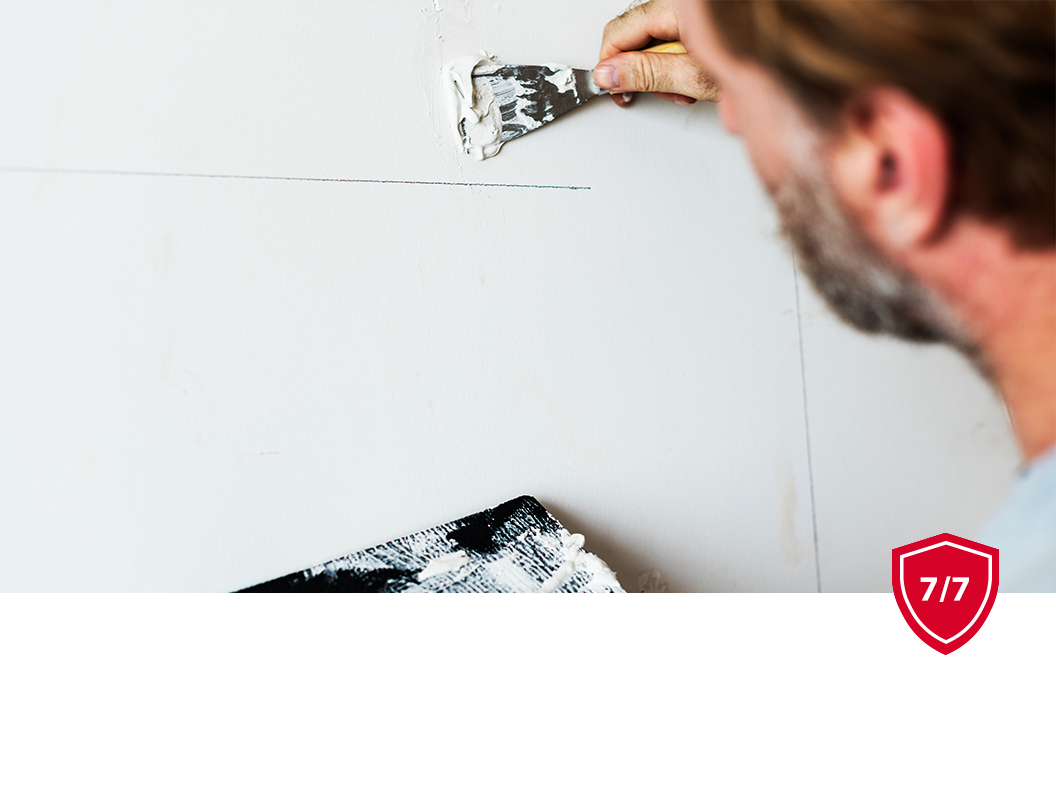 A person using a metal putty knife to apply white spackle to a wall.