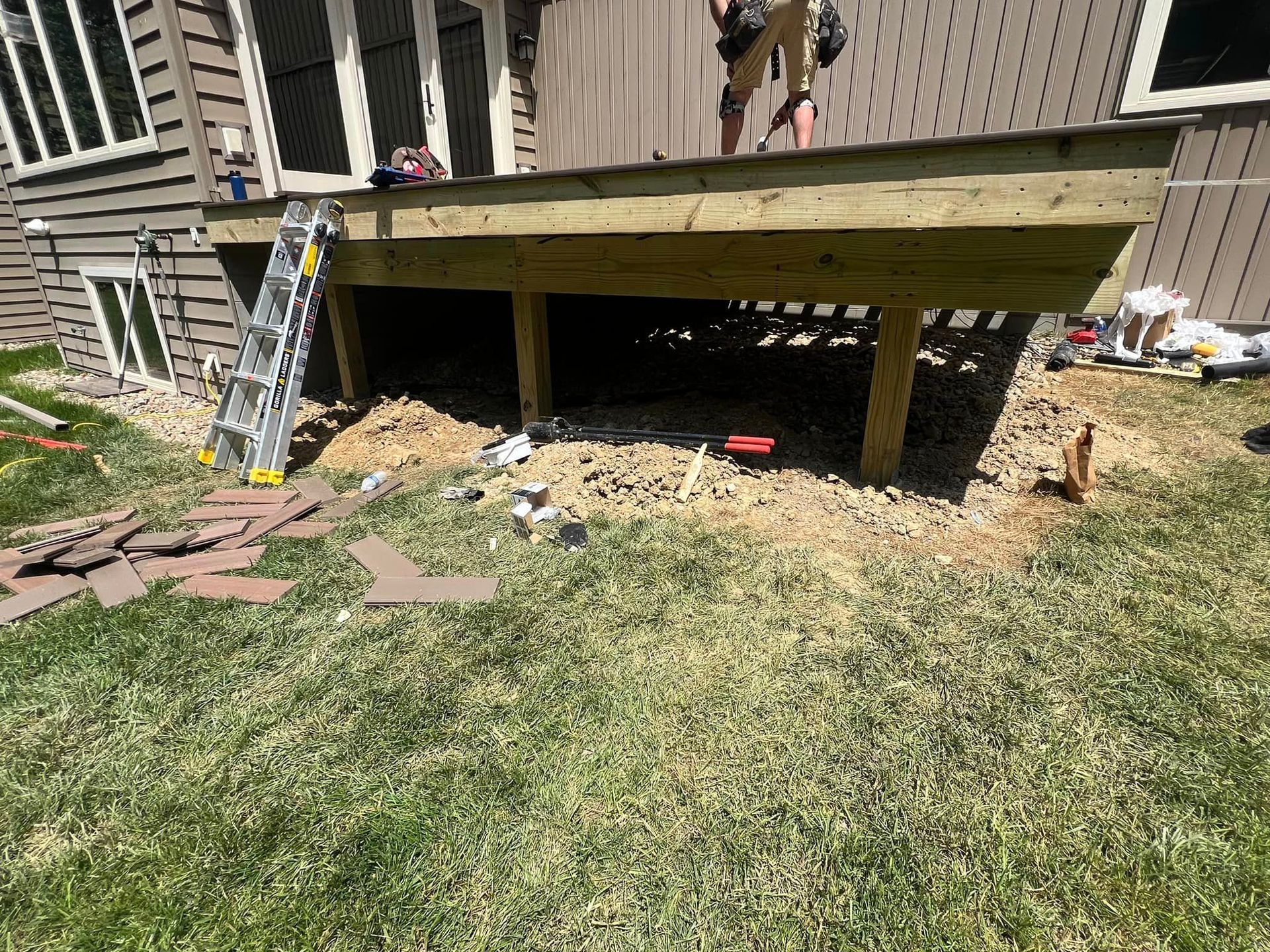Construction of a wooden deck attached to a house, with a ladder leaning against it and building materials on the lawn.