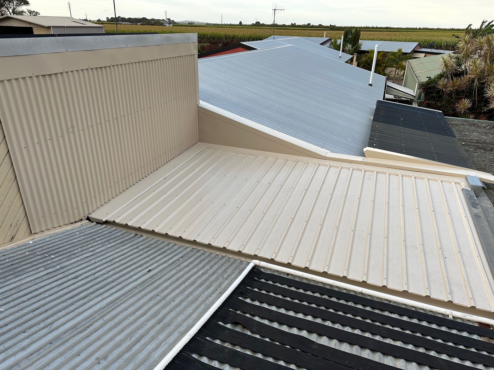Rooftops with corrugated metal panels and a curved white roof under an overcast sky.