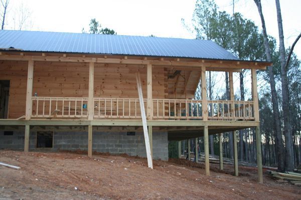 Wooden cabin under construction with porch and metal roof.