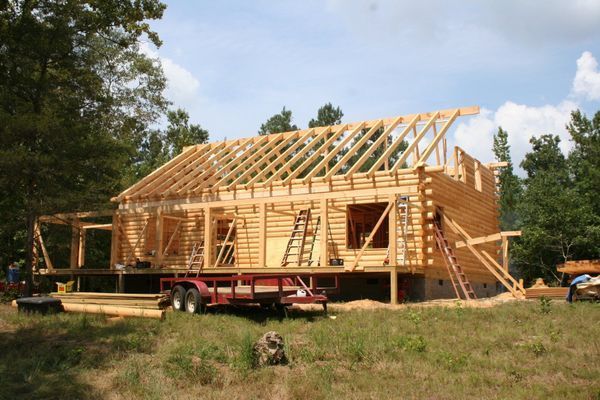 Log cabin under construction with exposed wooden frame and rafters.