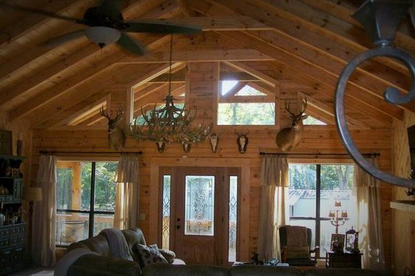 Wooden cabin interior with chandelier, mounted deer heads, and windows with outdoor views.