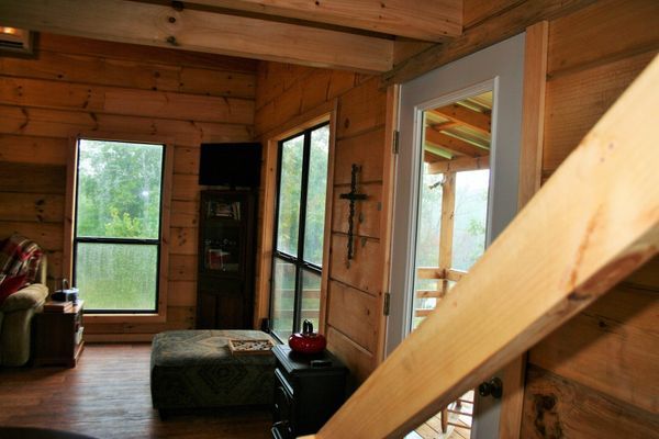 Interior of a wood-paneled cabin with windows, a door, and a staircase.