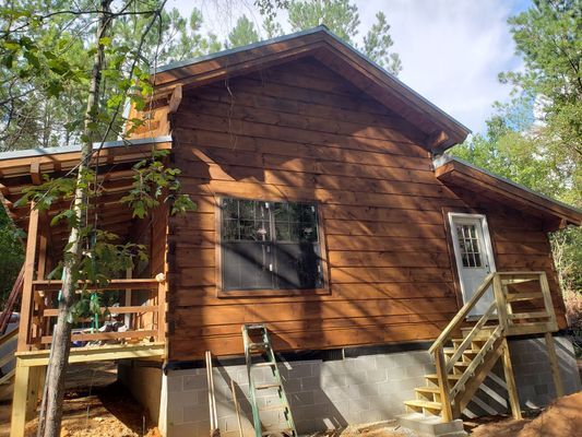 Brown log cabin with wooden deck and stairs.