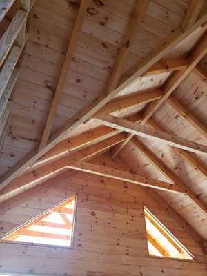 Interior view of unfinished wooden structure with triangular windows and rafters.