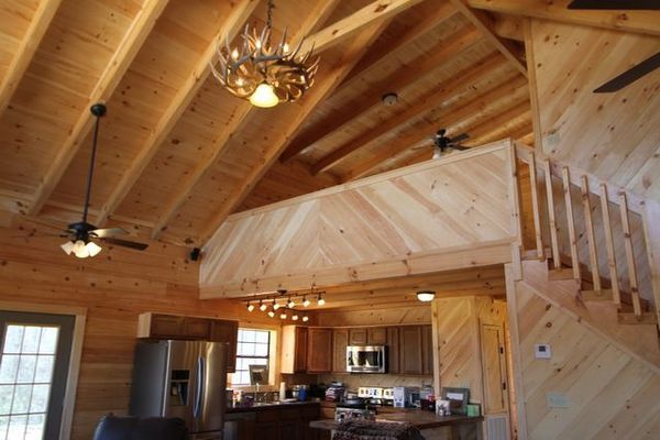 Interior of a cabin with wooden walls and ceiling, loft, staircase, and kitchen visible.