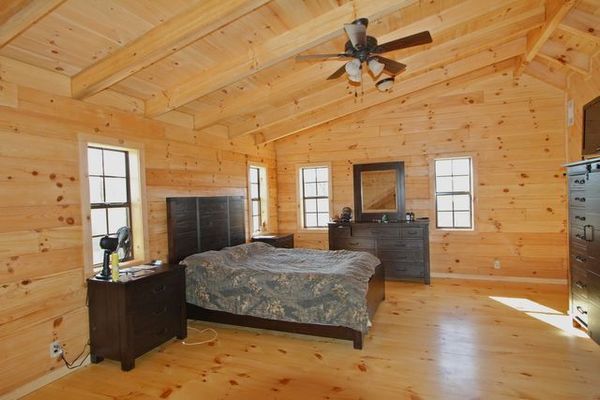 Bedroom with wood paneled walls, floor, and ceiling. Features a bed, dresser, and three windows.