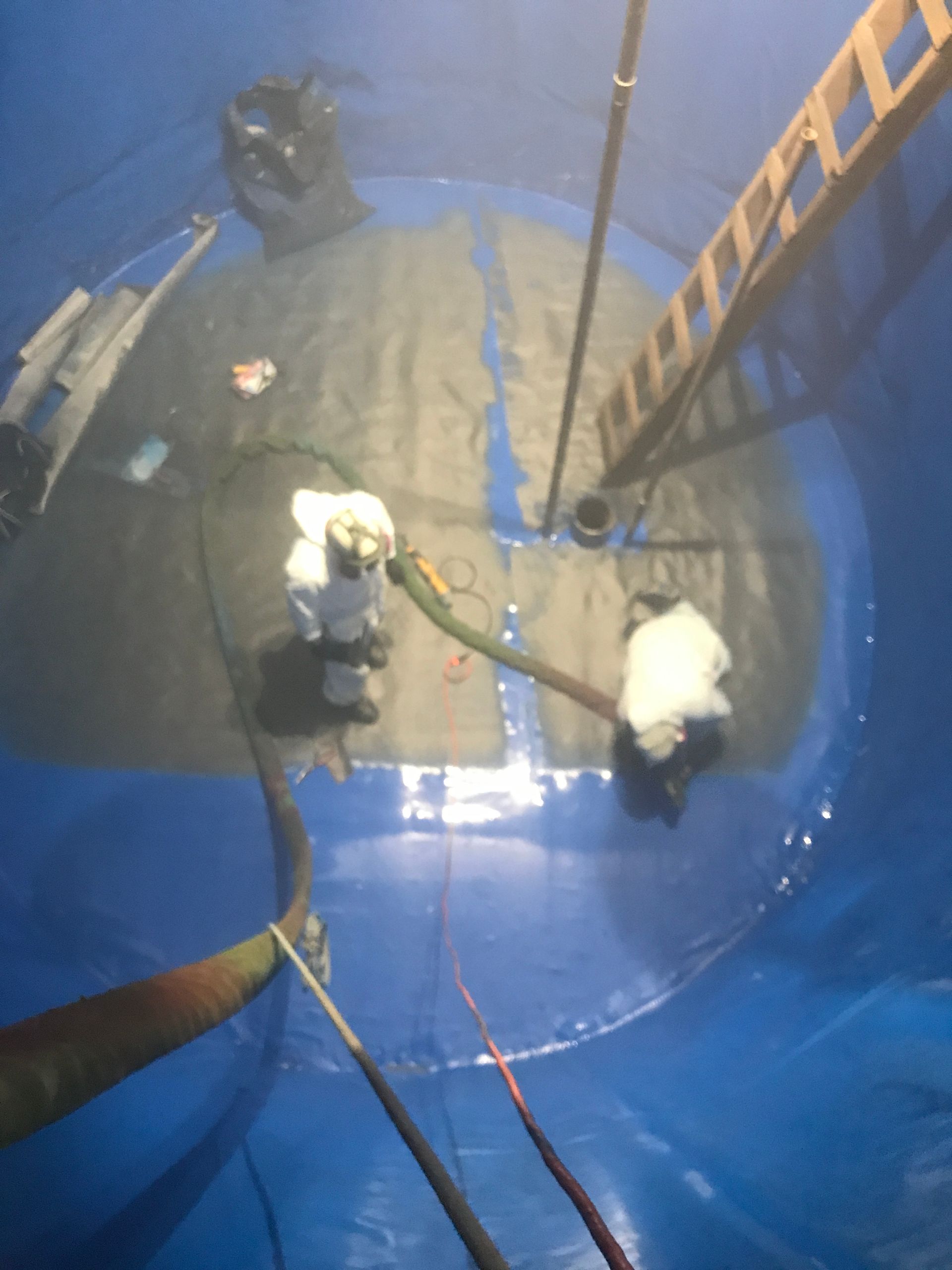 A man is working on a large blue tank with a ladder