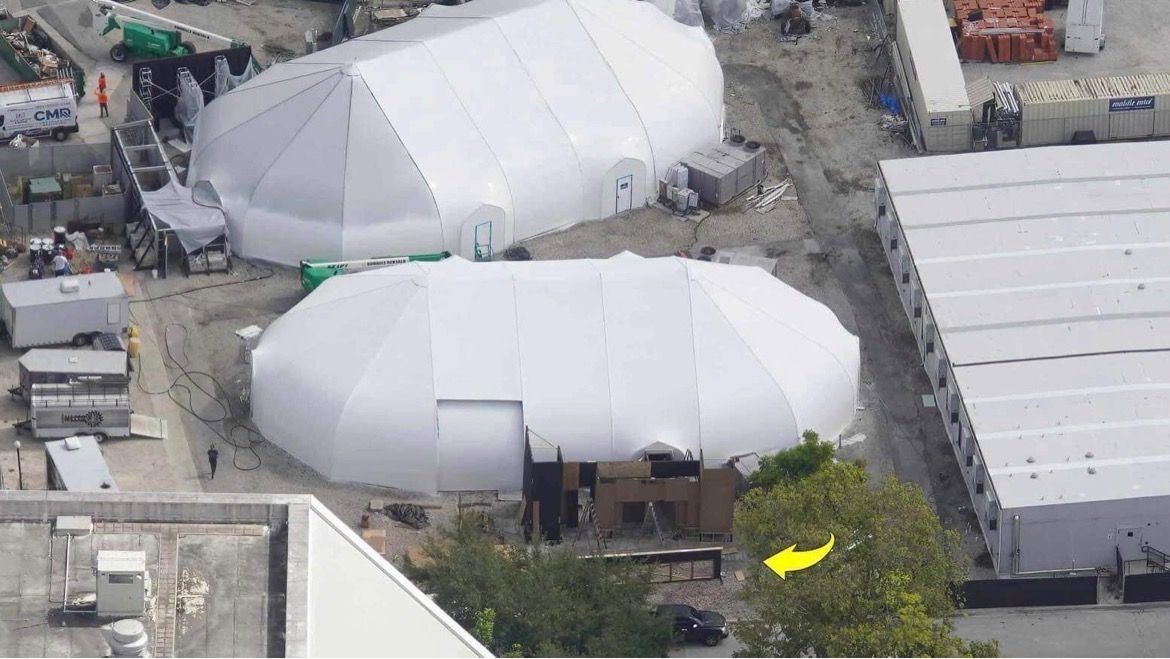 An aerial view of a large white tent with a yellow arrow pointing to it