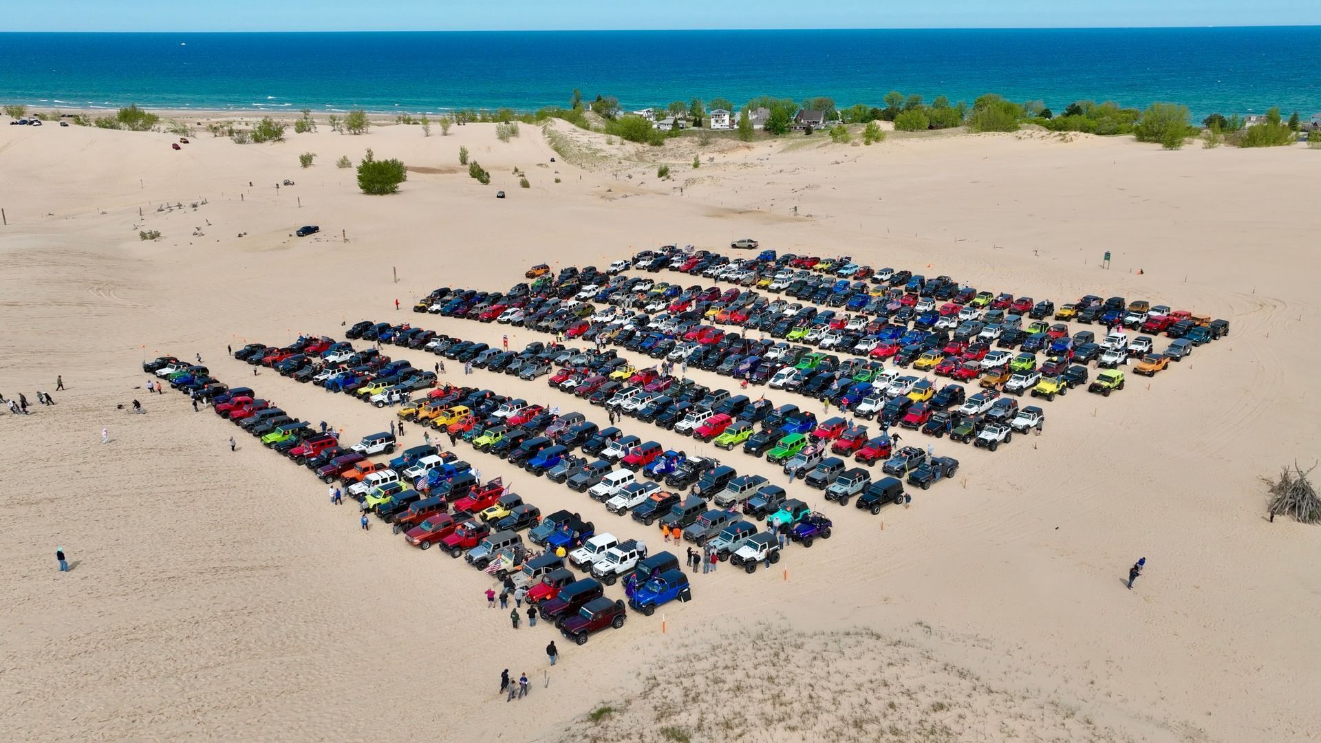 Cars parked in rows on a sandy beach, likely for a car show, near the ocean.