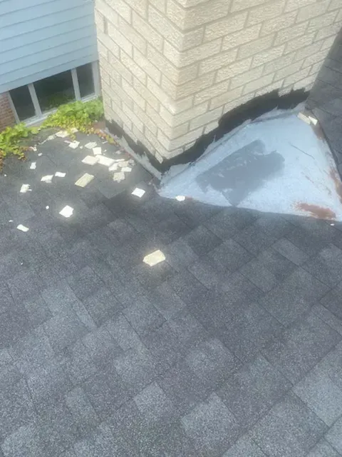 Roof shingles with scattered debris near a brick wall and blue metal flashing by a window