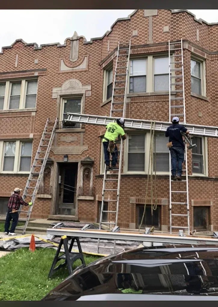 Workers on ladders repairing the brick facade of a townhouse building