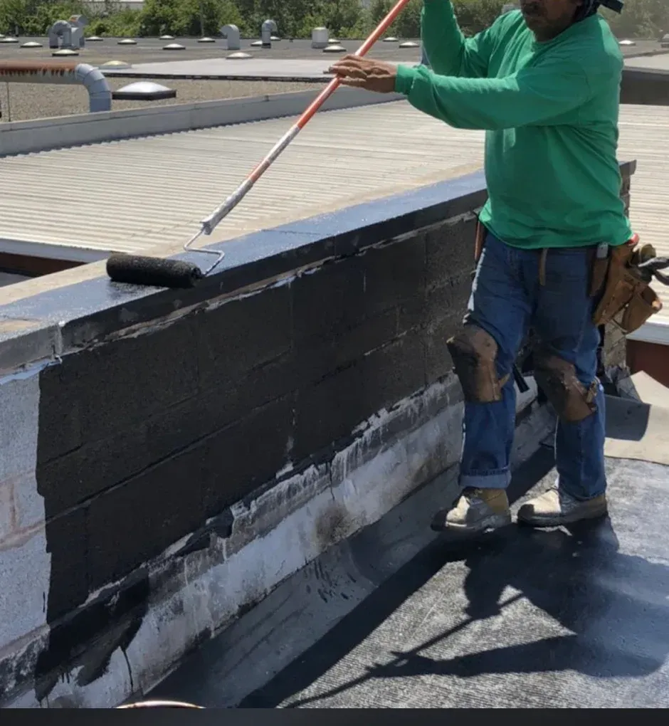 Worker painting a rooftop parapet wall black with a roller