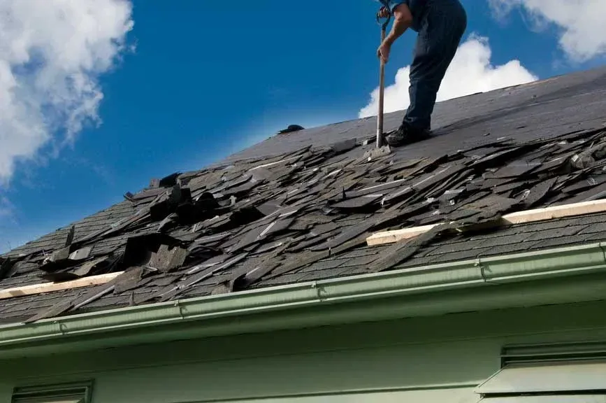 Worker repairing damaged shingles on a steep roof under a blue sky