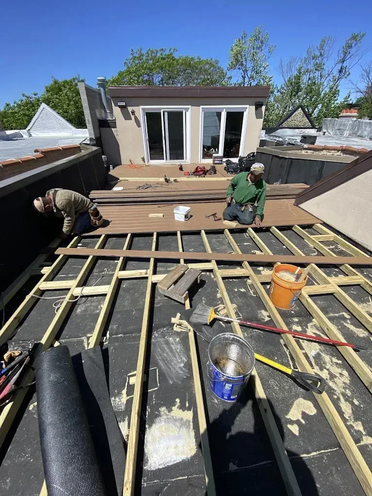 Roofers installing wood framing on a flat roof beside a small house on a sunny day