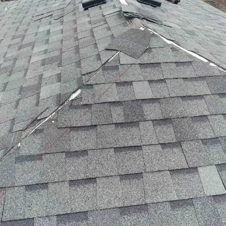 Damaged gray shingle roof with missing and curled shingles near the ridge