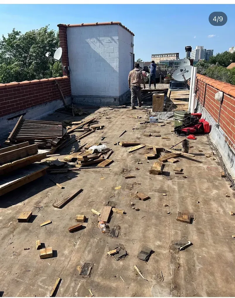Rooftop under repair with workers, scattered wood planks, and a partly removed roof surface.