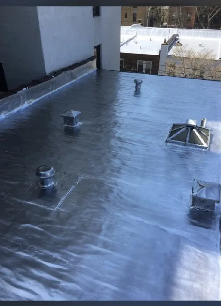 Rooftop with silver membrane roofing, vents, and a white parapet wall in winter light